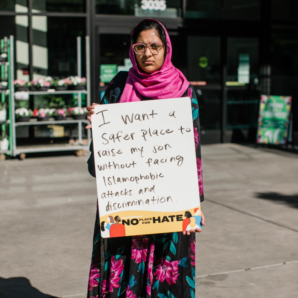 Image of a woman in a hijab holding a sign that reads, "I want a safer place to raise my son without facing Islamophobic attacks and discrimination."