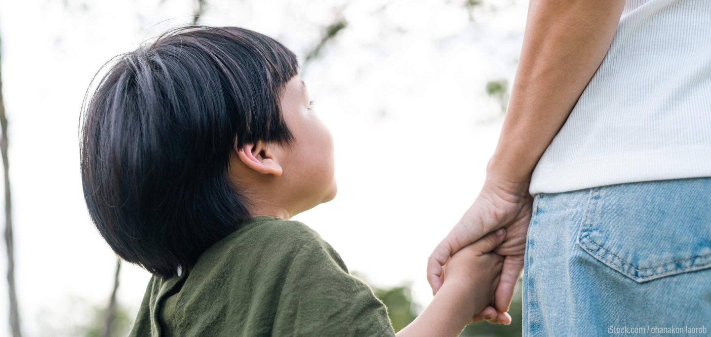 Young East Asian boy holds onto parent's hand.